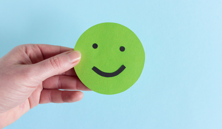 Closeup of round happy smiley of green color in crop hand against blue background 