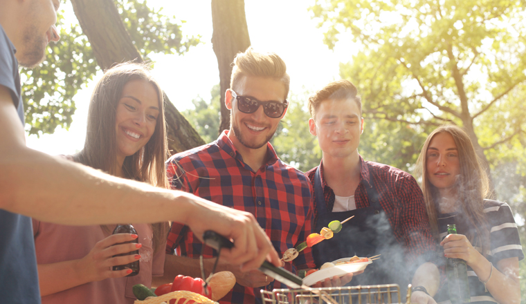 Happy friends grilling meat and enjoying barbecue party outdoors