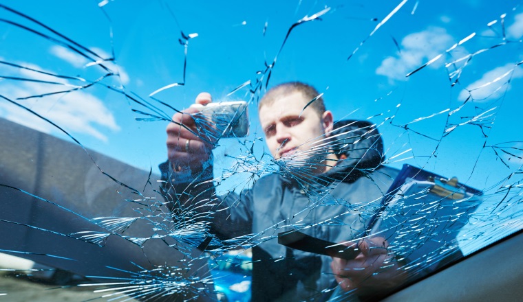 Insurance agent recording damage after car windscreen crash during inspecting damaged automobile on claim form