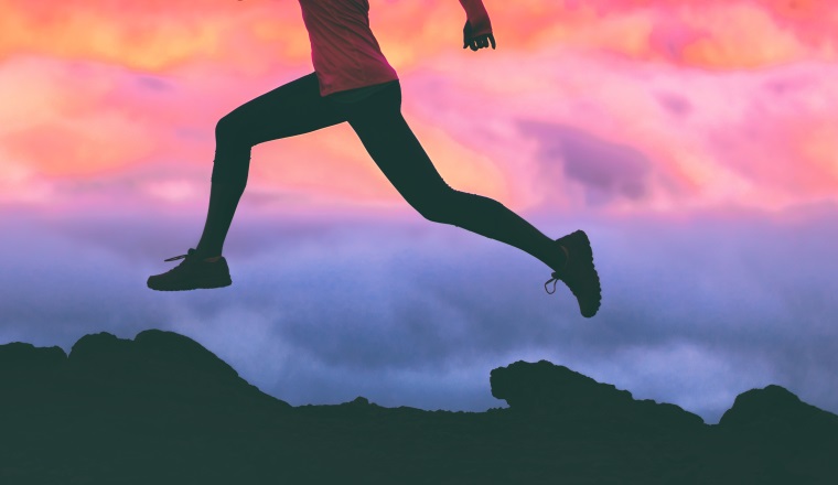 Running legs silhouette of athlete runner woman trail running on mountain rocks against pink sunset sky background. Panoramic banner.