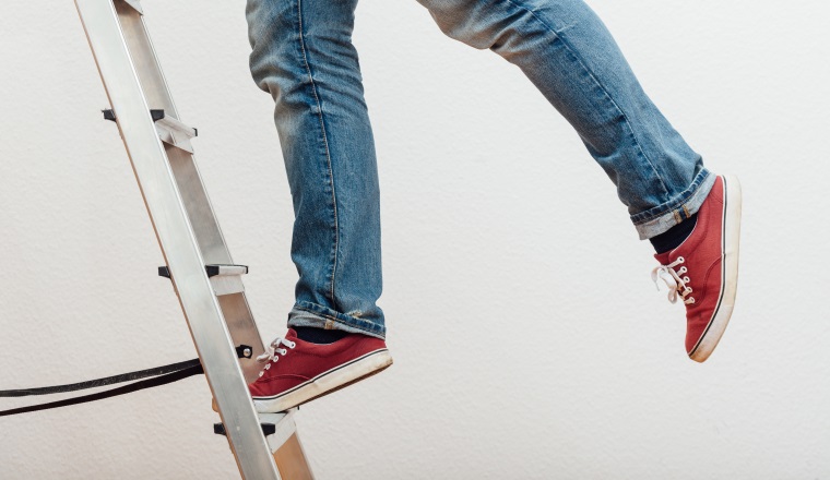Anonymous man reaching on top of ladder climbing, indoors studio people shot.