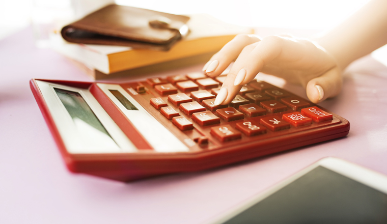 woman is holding purse, credit card in hands and calculating the costs. Pink table. Flowers on the table. hand holding brown purse. Red calculating.