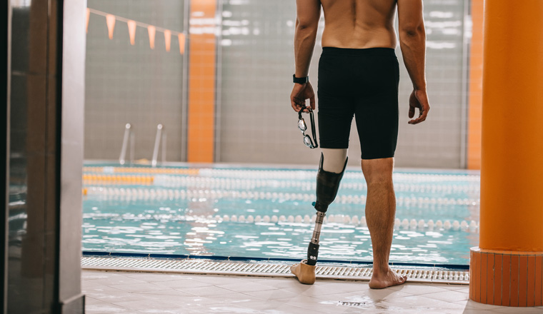cropped shot of sportsman with artificial leg standing in front of indoor swimming pool