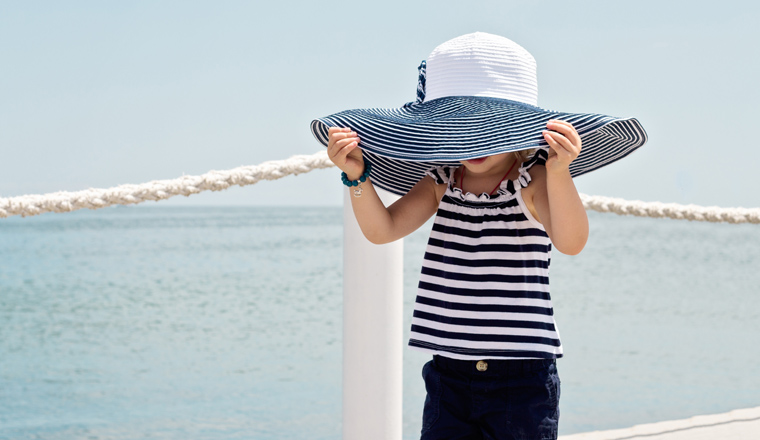 Funny little girl (3 years) in big hat on the beach. Selective focus.