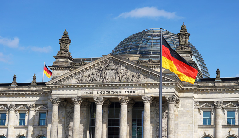 German flag waving at Bundestag building in Berlin Germany front facade view in a sunny day with blue sky.