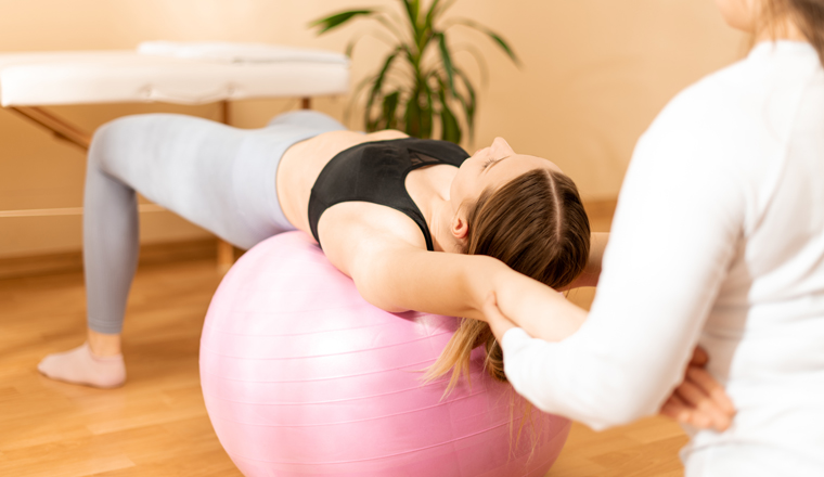 Physiotherapist working with young female client on core strength using fitball. Rehabilitation and physiotherapy background.