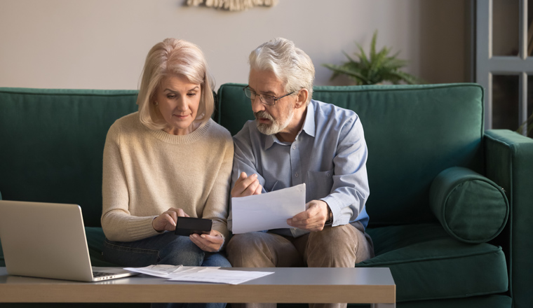 Serious mature couple calculating bills to pay, checking domestic finances, middle aged family managing, planning budget, expenses, grey haired man and woman reading bank loan documents at home