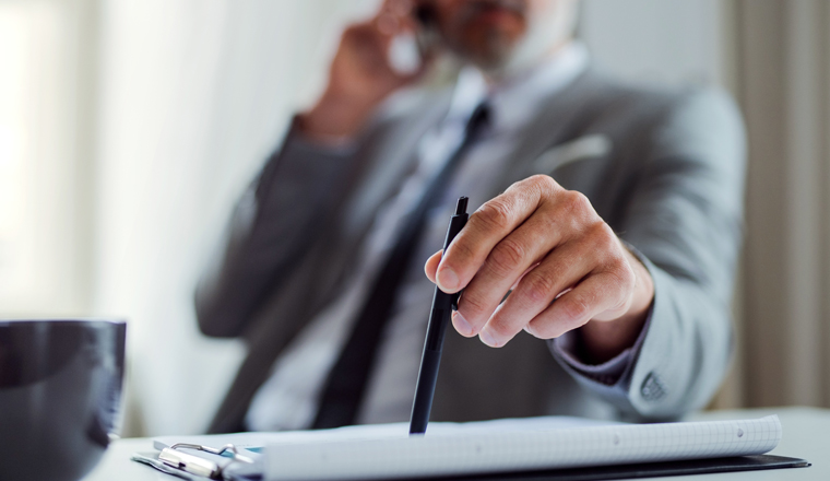 A midsection of unrecognizable businessman with smartphone sitting at the table in an office, making a phone call.