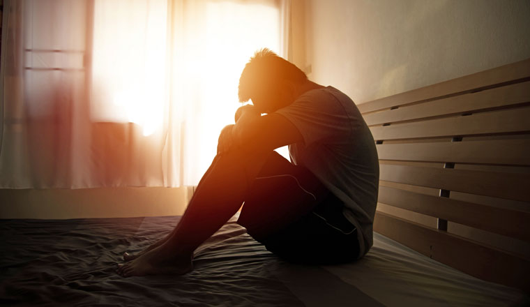 desperate man in silhouette sitting on the bed with hands on head