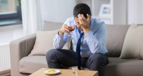 alcoholism, alcohol addiction and people concept - male alcoholic drinking brandy and smoking cigarette at home